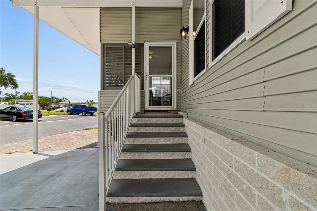 Exterior view of a home entrance with concrete steps leading to a glass storm door — 9790 66TH STREET N UNIT 252, PINELLAS PARK, FL