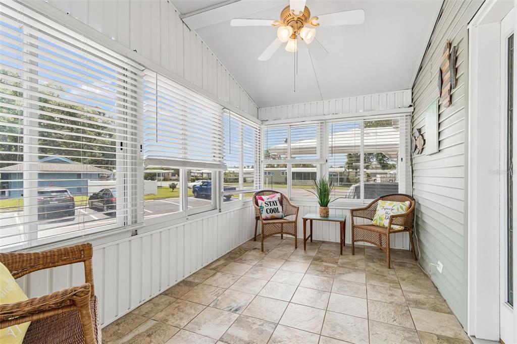 A sunroom features tiled floors, wicker chairs, large windows with blinds, and a ceiling fan — 9790 66TH STREET N UNIT 252, PINELLAS PARK, FL