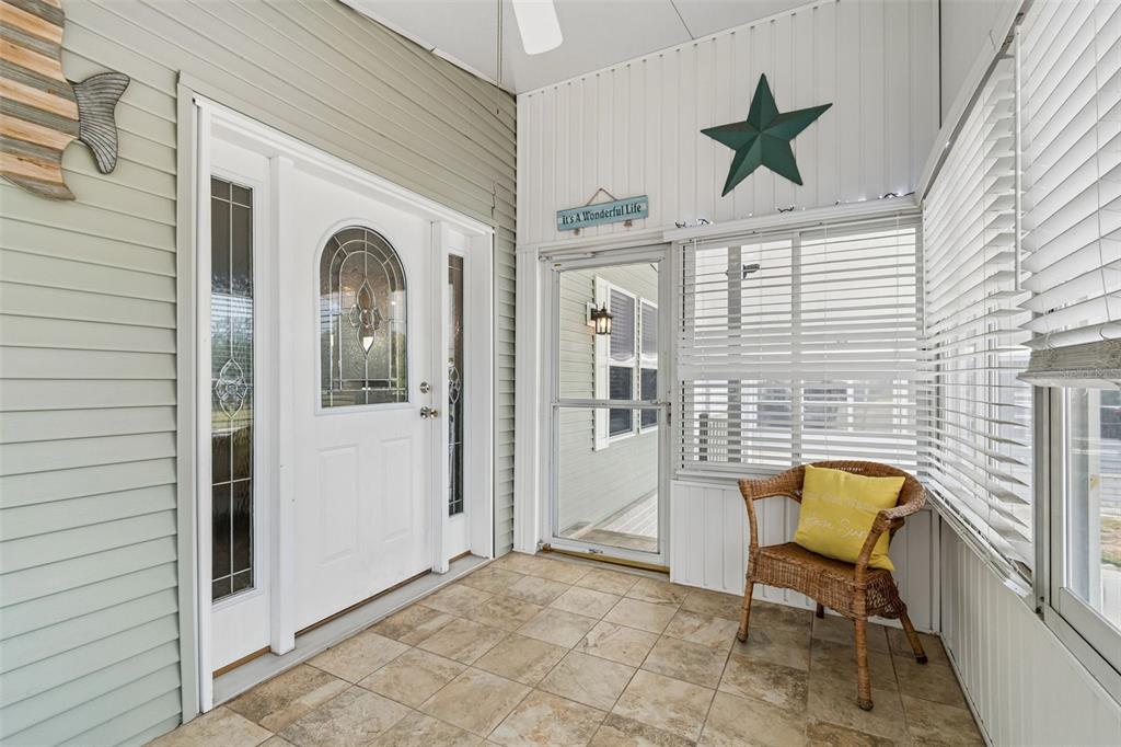 A covered porch features tile flooring, a white front door, and a wicker chair — 9790 66TH STREET N UNIT 252, PINELLAS PARK, FL