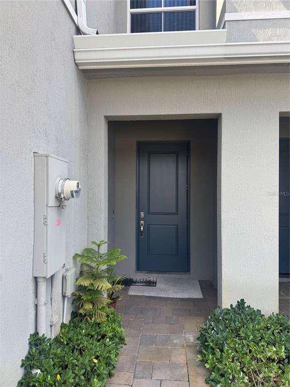A gray front door is recessed within a stucco entryway featuring a paved walkway — 176 BANDOL STREET, WEST PALM BEACH, FL