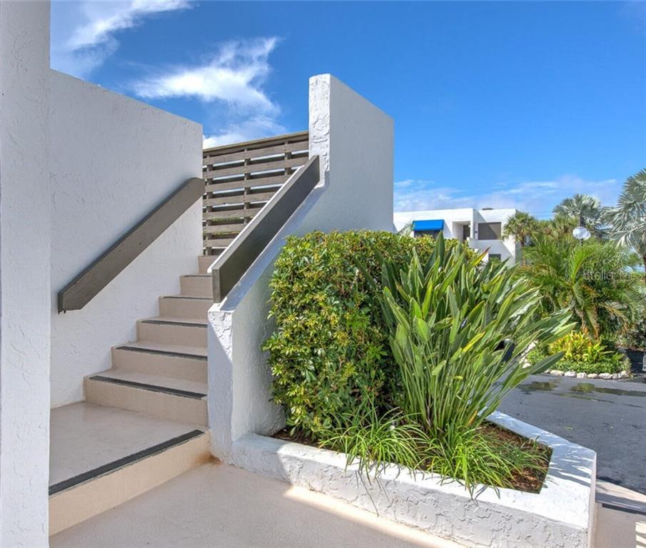 An outdoor staircase with a wooden handrail leads up beside a white stucco wall and planter — 522 BAYPORT WAY UNIT 522, LONGBOAT KEY, FL