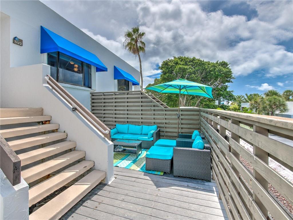 An outdoor deck features a staircase, blue patio furniture, and a striped umbrella — 522 BAYPORT WAY UNIT 522, LONGBOAT KEY, FL