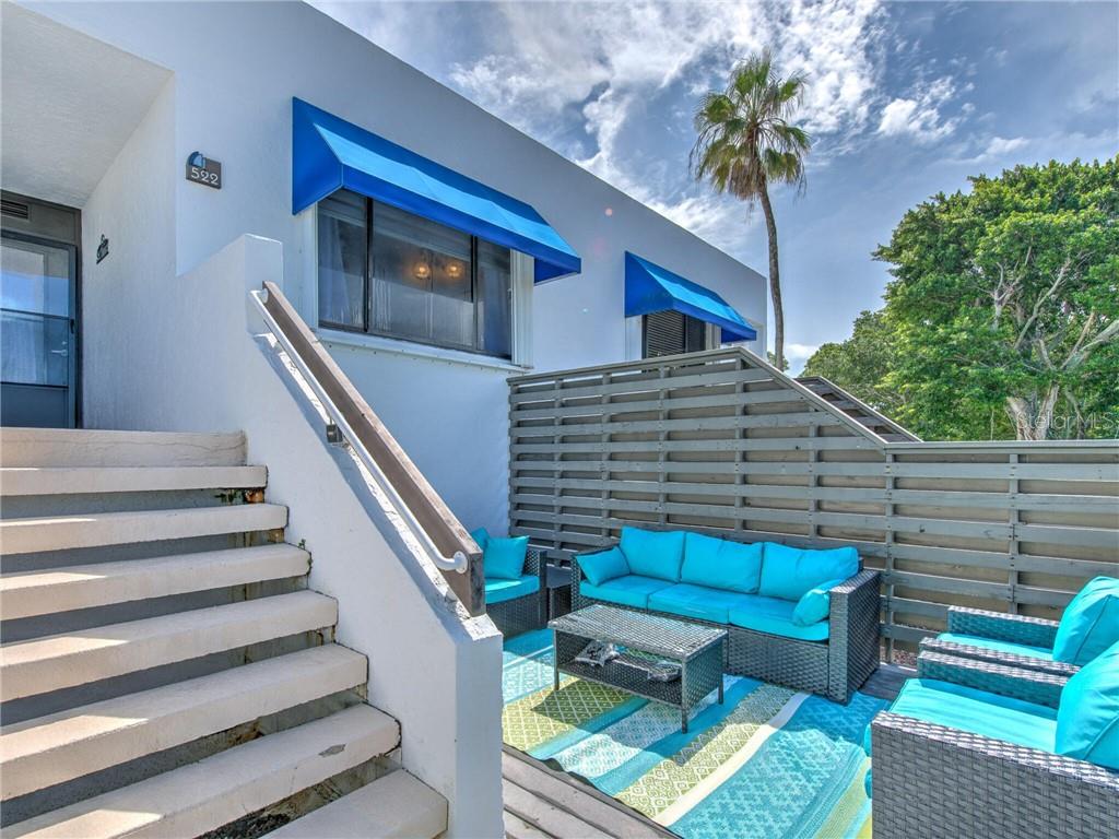 An outdoor patio features wicker furniture with bright blue cushions and a patterned area rug — 522 BAYPORT WAY UNIT 522, LONGBOAT KEY, FL