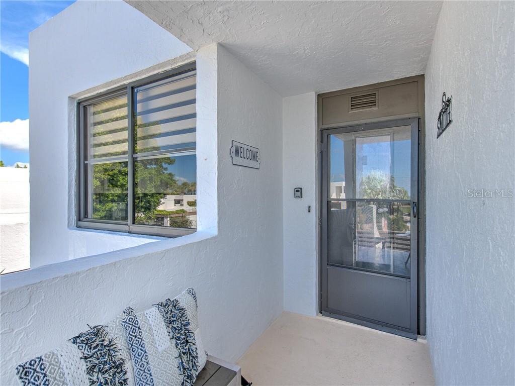A white-walled entryway features a screen door, a window, and a bench with patterned pillows — 522 BAYPORT WAY UNIT 522, LONGBOAT KEY, FL