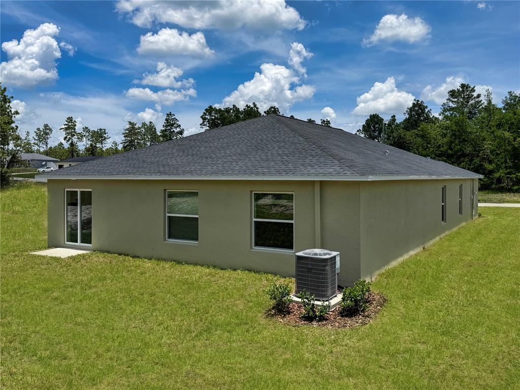 The rear exterior of a tan, single-story house features a gray roof and air conditioner — 13121 SW 86TH COURT, OCALA, FL