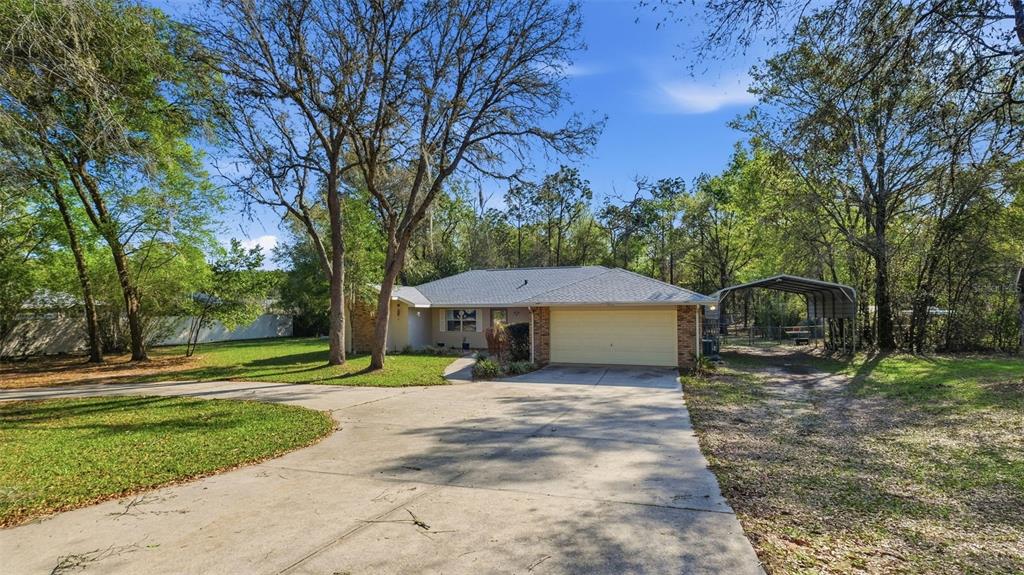 A single-story house with a two-car garage, a metal carport, and a large concrete driveway — 12435 S CANNA POINT, FLORAL CITY, FL