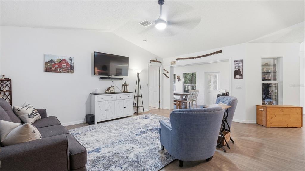 A living room features a gray sofa, two blue armchairs, a television, and wood-look flooring — 12435 S CANNA POINT, FLORAL CITY, FL