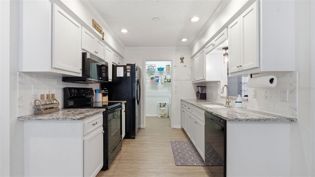A galley kitchen features white cabinets, granite countertops, and black appliances — 12435 S CANNA POINT, FLORAL CITY, FL