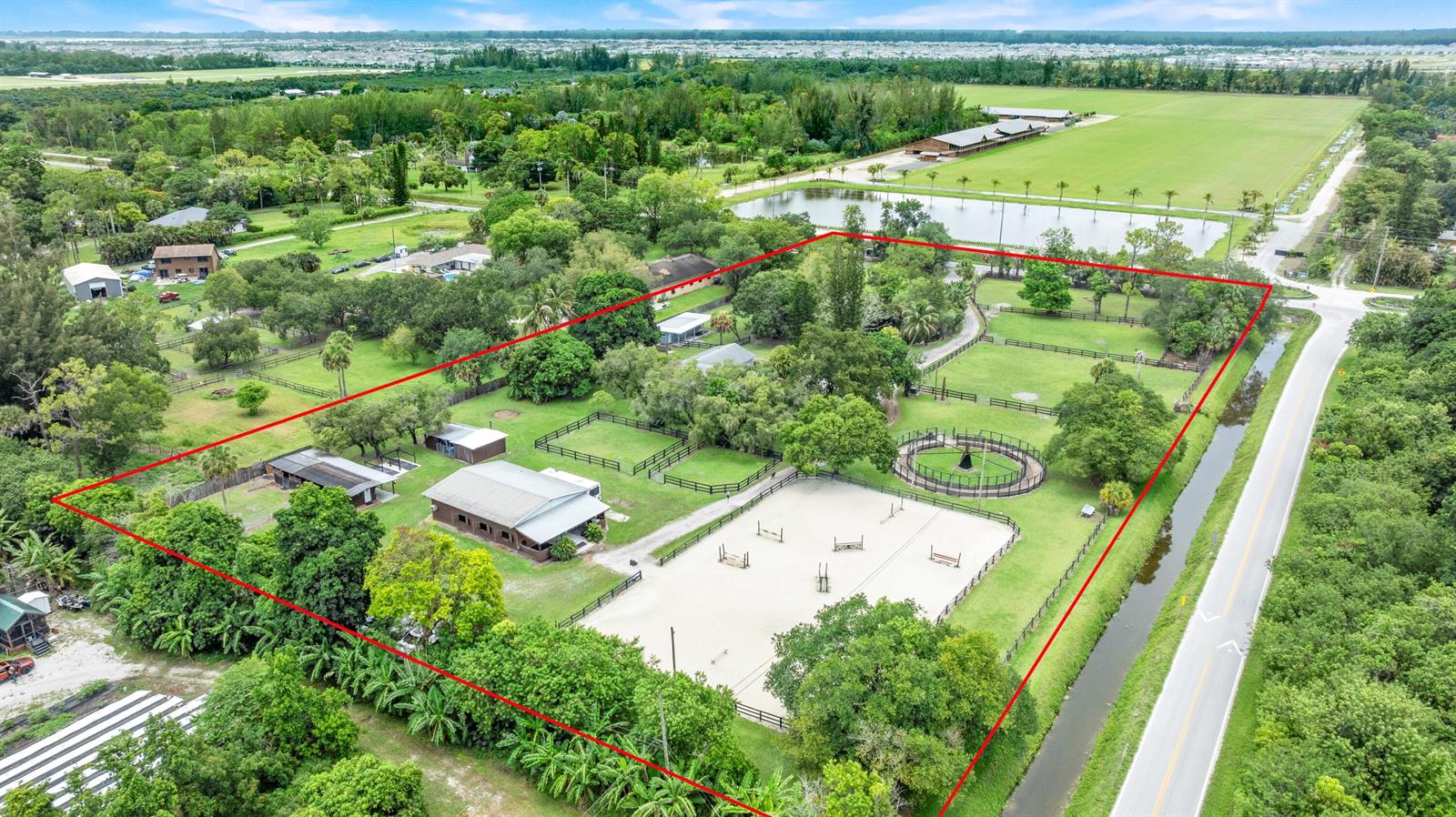 An aerial view shows a fenced equestrian property with a riding arena, stables, and trees — 14536 North Road, FL 33470, FL
