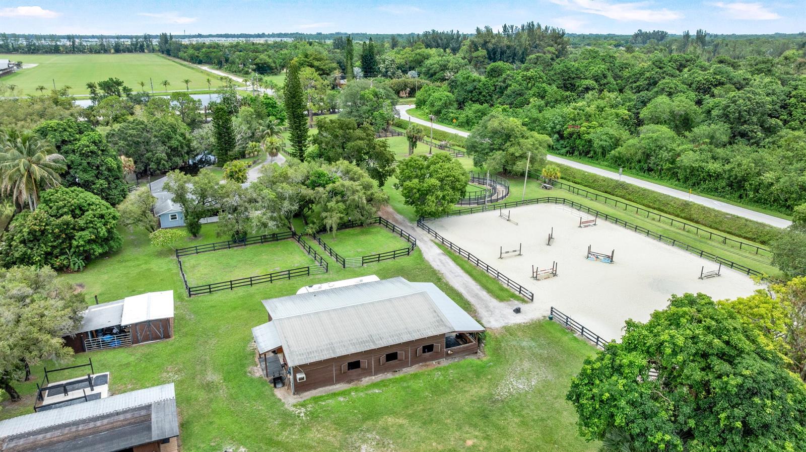 An aerial view shows a horse stable, a riding arena, and fenced paddocks on property — 14536 North Road, FL 33470, FL