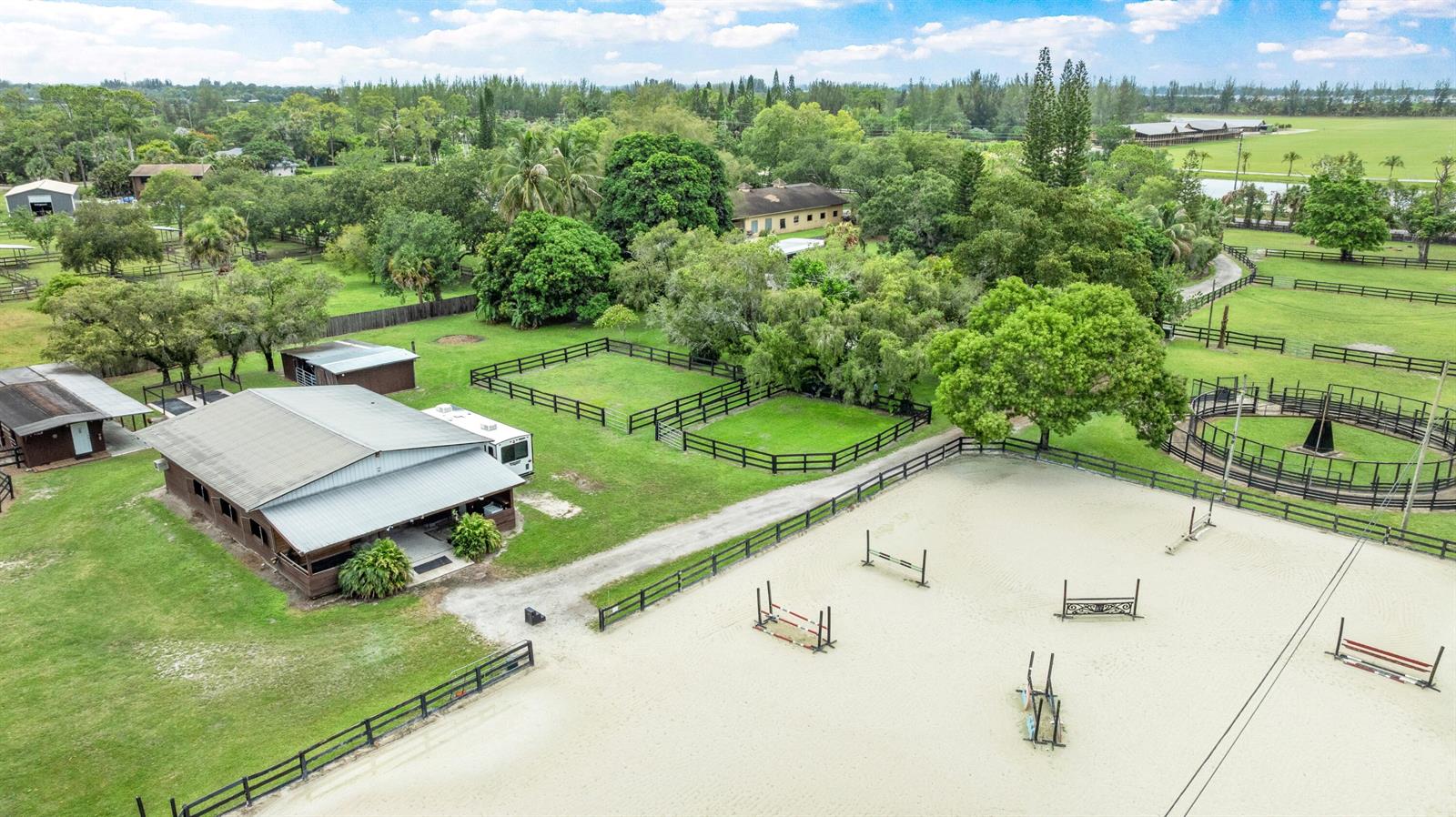An aerial view shows a horse stable, a riding arena with jumps, and fenced paddocks — 14536 North Road, FL 33470, FL