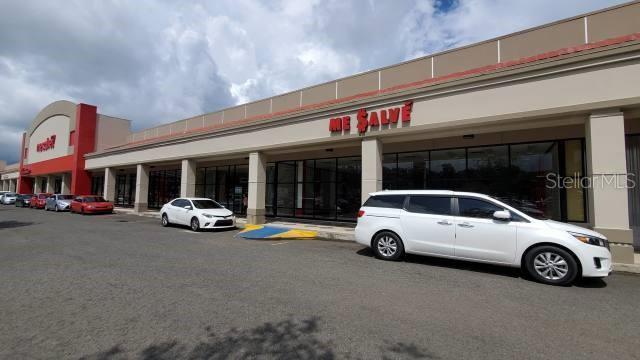 A white minivan is parked in front of a commercial strip mall with storefronts — 14 PR-14 KM 52.7, AIBONITO, PR