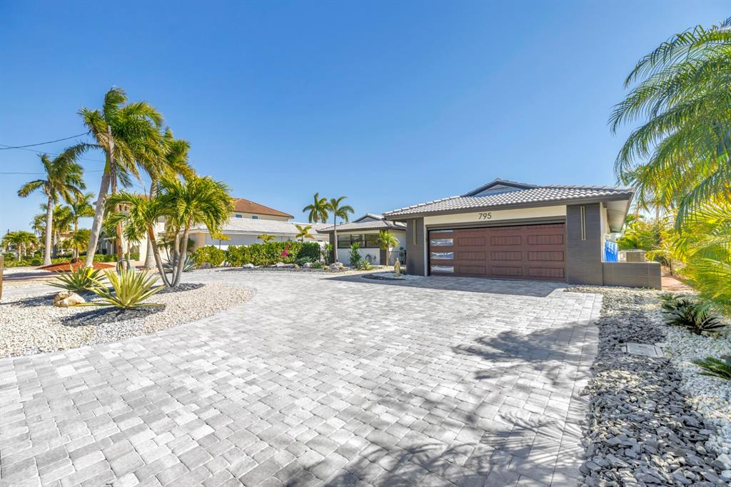 A house exterior features a paved driveway, a brown garage door, and palm trees — 795 CAPRI BOULEVARD, TREASURE ISLAND, FL