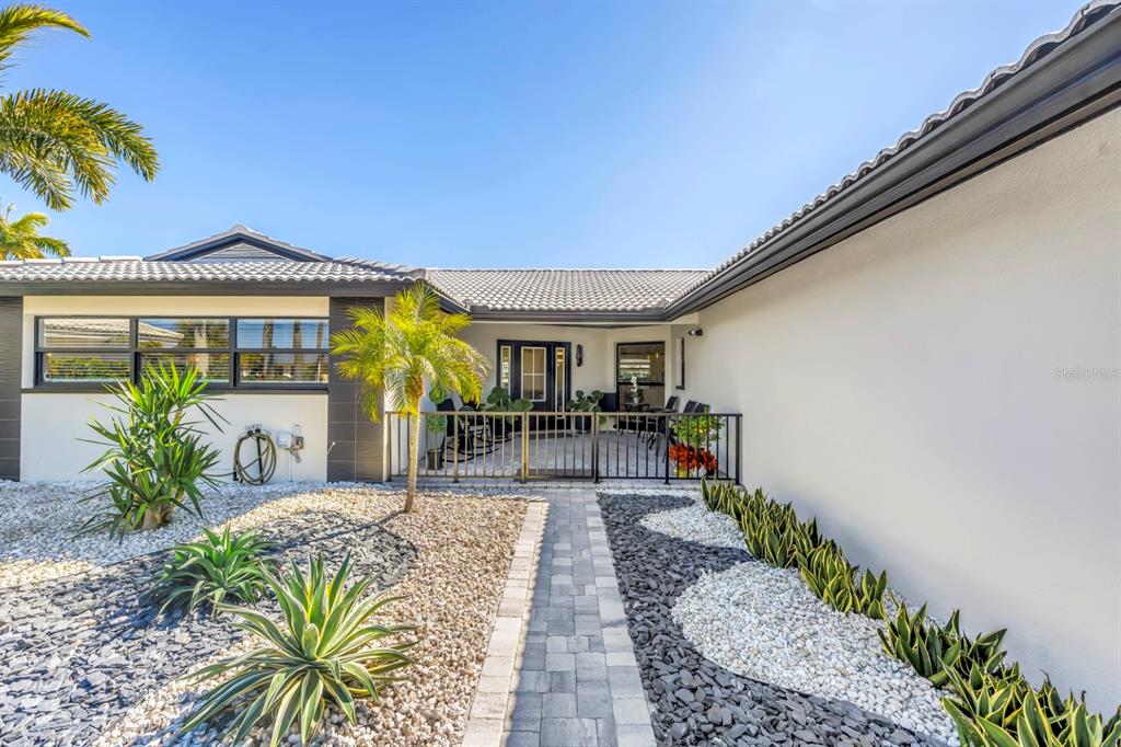 A paved walkway leads to a gated courtyard entrance of a house with xeriscaped landscaping — 795 CAPRI BOULEVARD, TREASURE ISLAND, FL