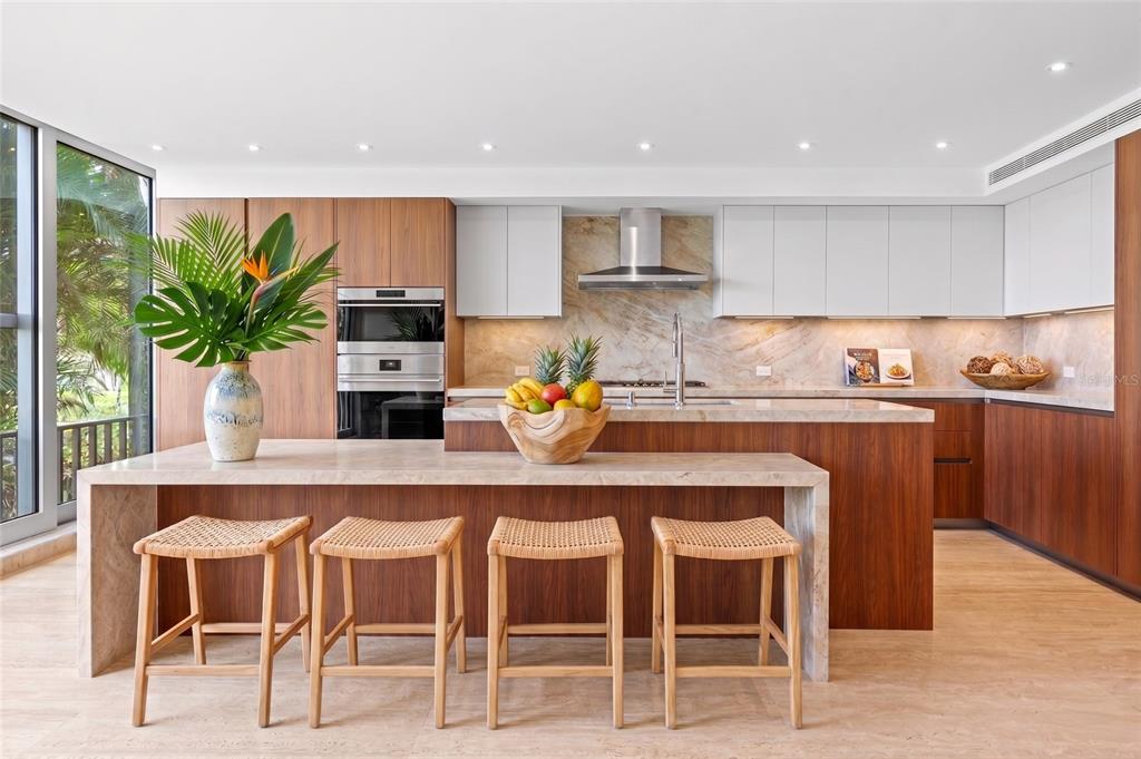 A modern kitchen features wood cabinetry, a stone island with four stools, and floor-to-ceiling windows — 2111-2112 VILLA DORADO BEACH ESTATES, DORADO, PR