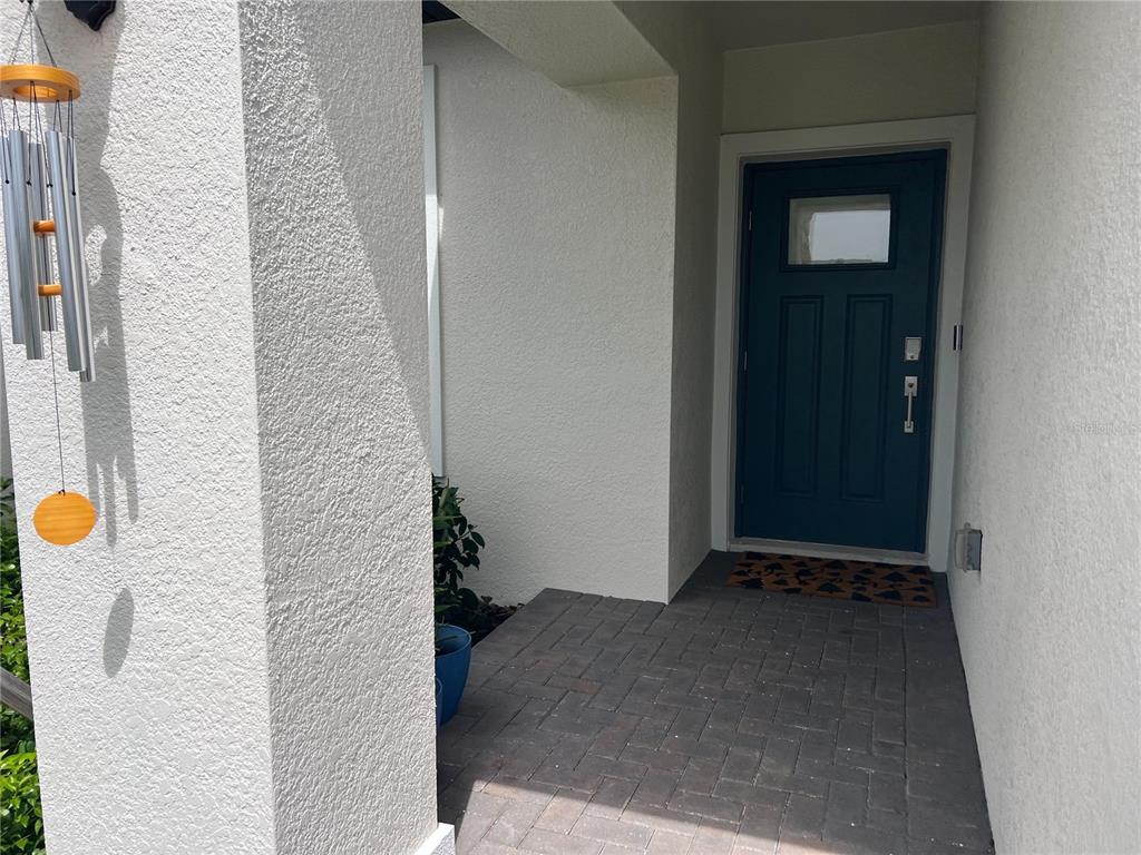 A covered entryway features a dark blue front door, a brick paver floor, and stucco walls — 32070 GRIFFIN SANDS LANE, SAN ANTONIO, FL