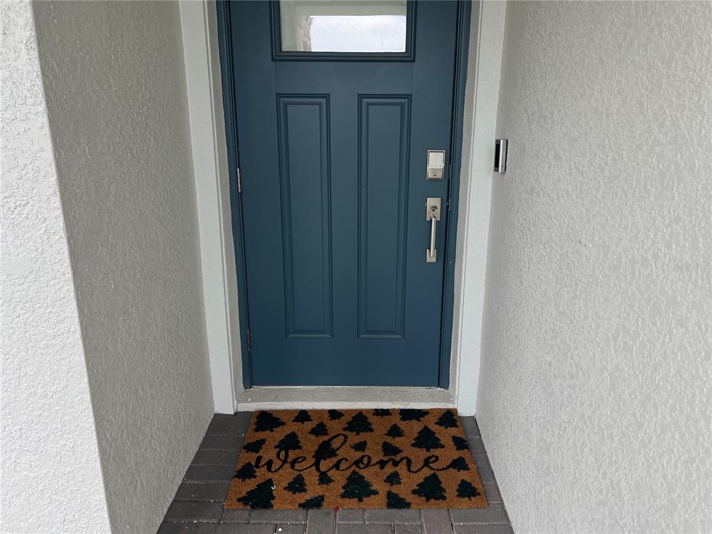A blue front door with a window and a welcome mat sits in a recessed entryway — 32070 GRIFFIN SANDS LANE, SAN ANTONIO, FL