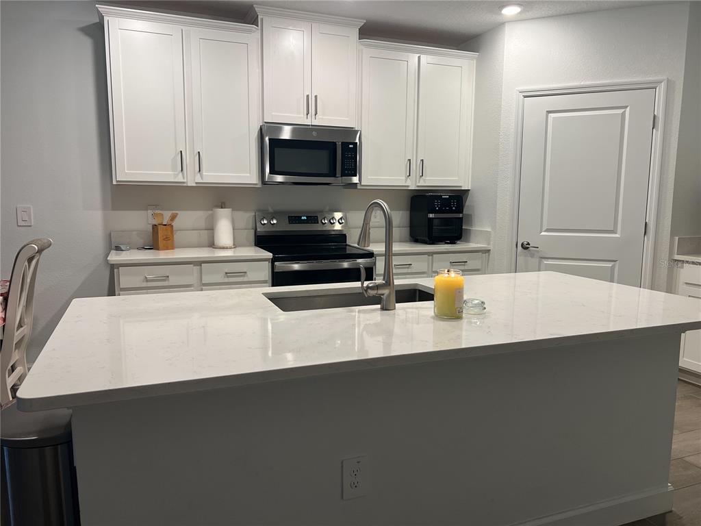 A kitchen features white cabinets, stainless steel appliances, and a large quartz-topped island — 32070 GRIFFIN SANDS LANE, SAN ANTONIO, FL