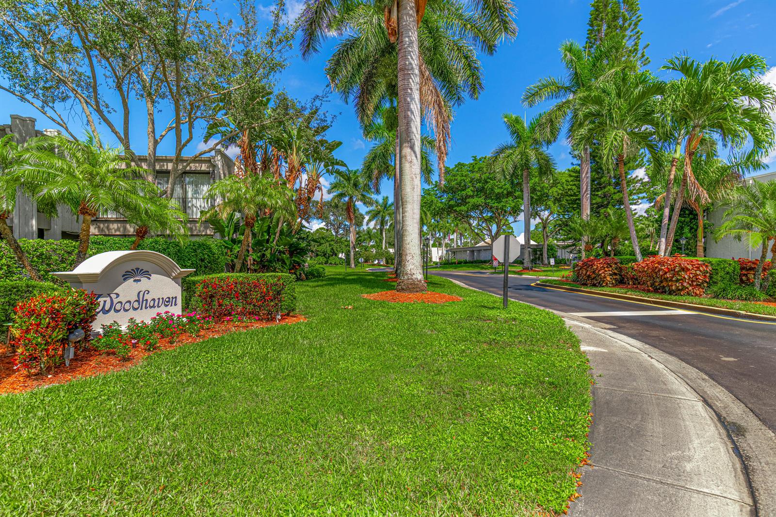 A stone sign for Woodhaven sits on a grassy lawn beside a palm-lined entrance road — 6548 Spring Bottom Way # 221, Boca Raton FL 33433, BOCA RATON, FL