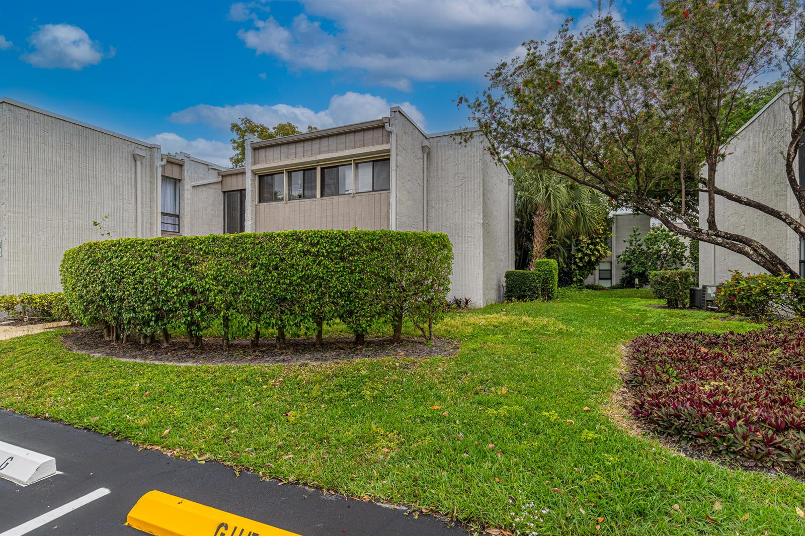 Exterior view of a multi-unit residential building with a manicured hedge and parking area — 6548 Spring Bottom Way # 221, Boca Raton FL 33433, BOCA RATON, FL