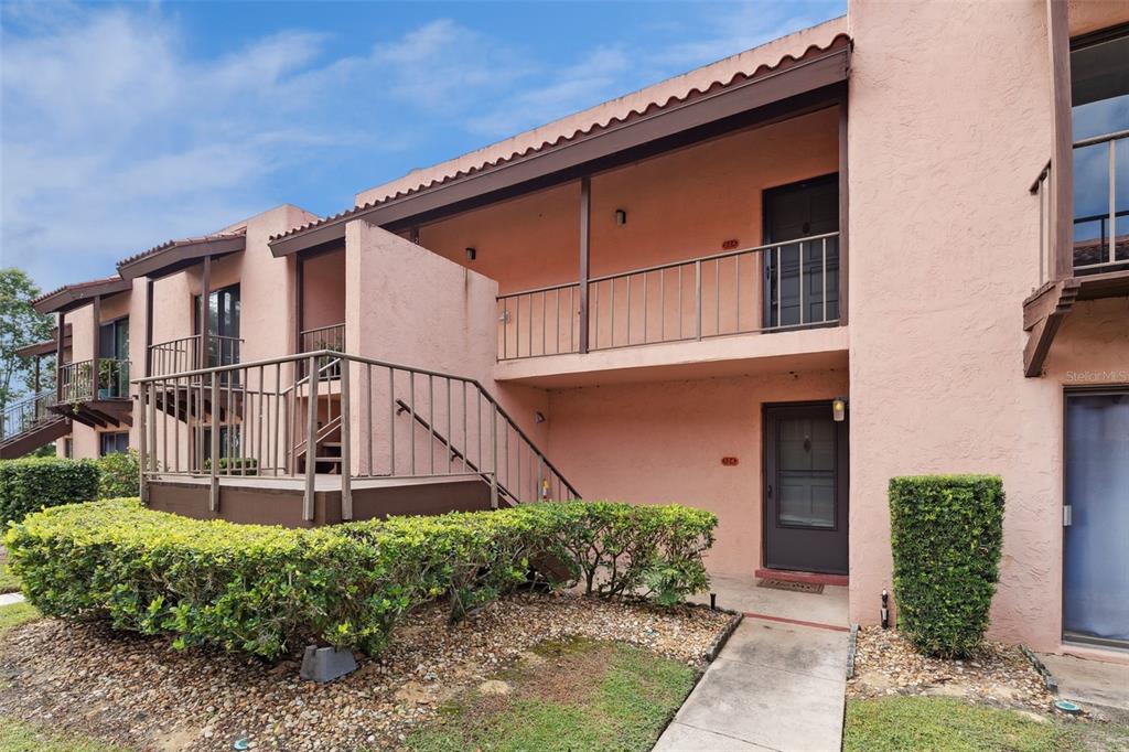 A two-story pink stucco apartment building features exterior staircases, metal railings, and landscaped bushes — 224 LA CASA UNIT 224, LAKE WALES, FL