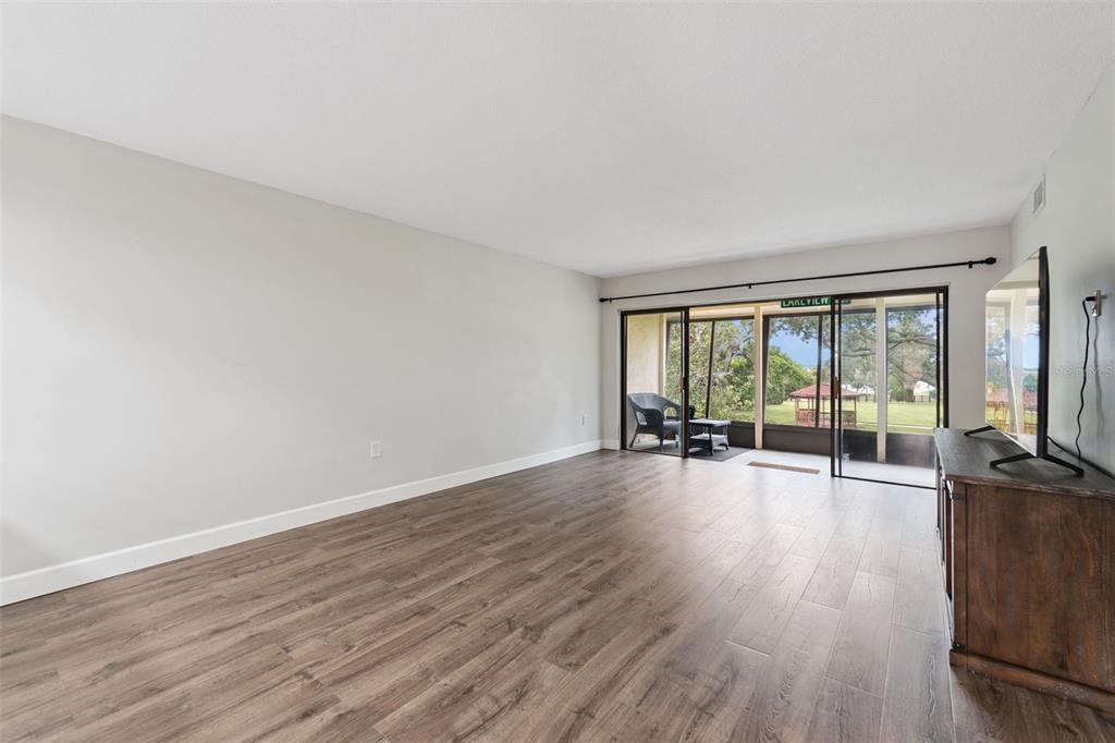 An empty living room with wood-look flooring, white walls, and sliding glass doors to a patio — 224 LA CASA UNIT 224, LAKE WALES, FL