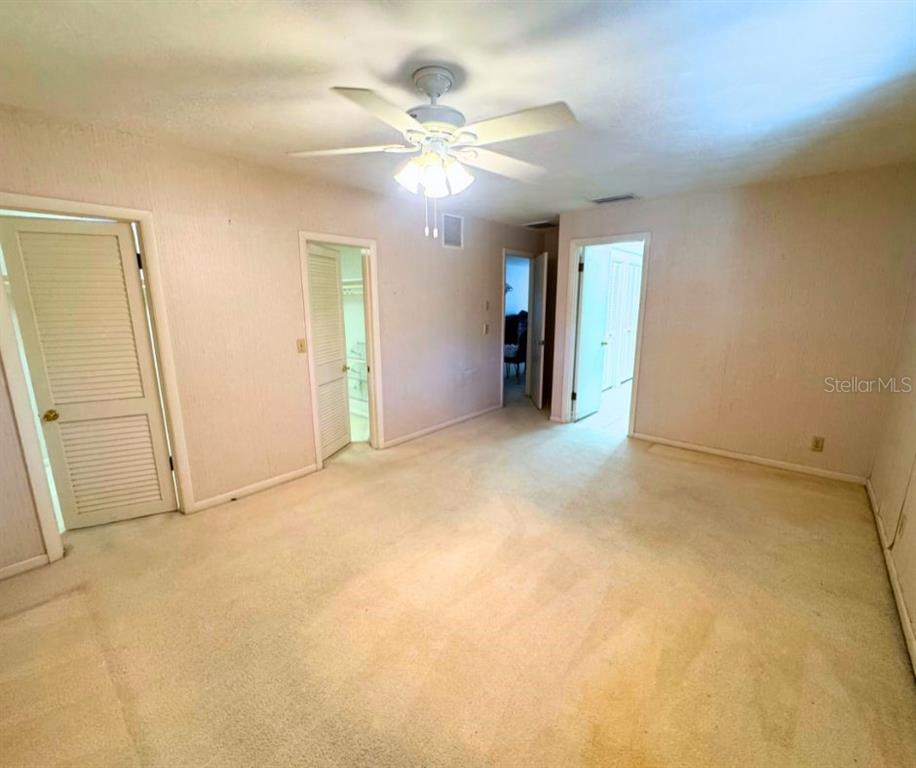A carpeted bedroom features a ceiling fan and three doorways leading to other rooms — 1505 N ARCADIA AVENUE, ARCADIA, FL