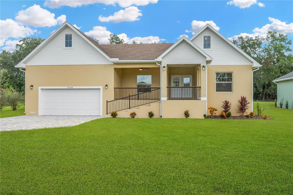 A single-story house with a tan stucco exterior, white siding, and a wheelchair ramp — 12500 GREEN OAK LANE, DADE CITY, FL