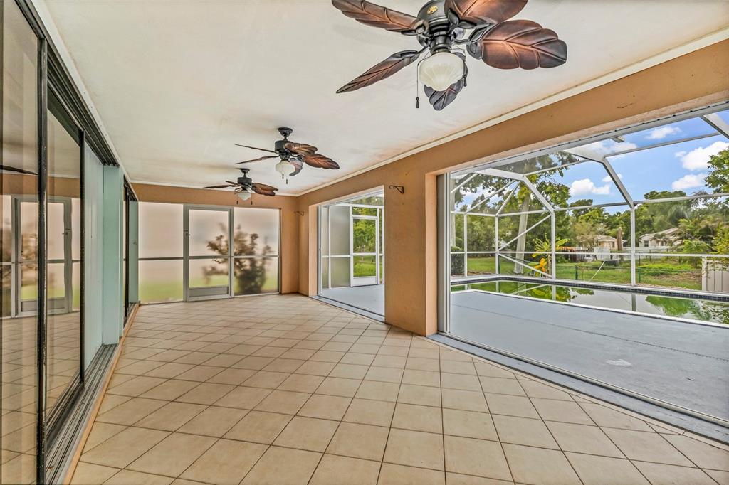 A tiled covered patio features two ceiling fans and sliding glass doors overlooking a pool enclosure — 2399 RIO DE JANEIRO AVENUE, PUNTA GORDA, FL
