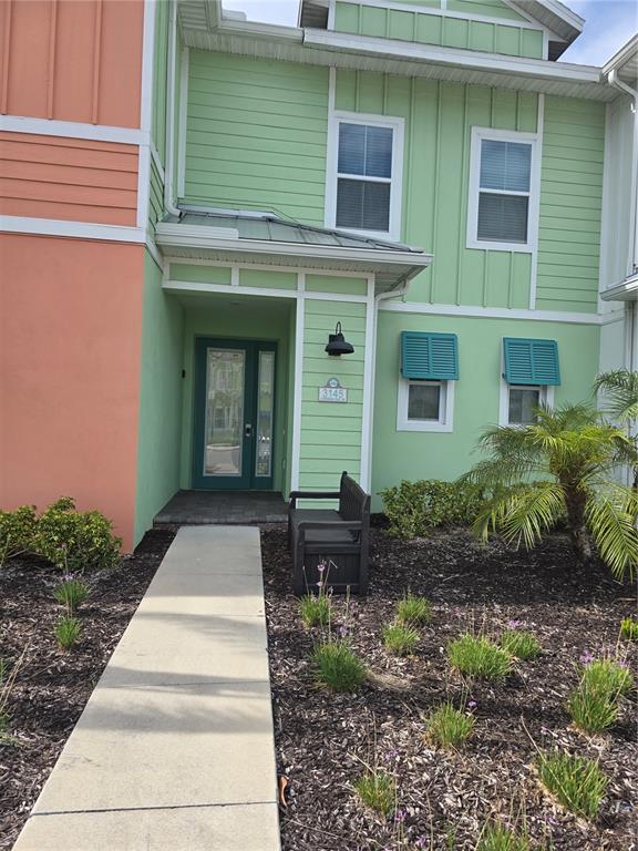 A light green two-story townhouse features a front entrance with a bench and landscaping — 3145 CARIBBEAN SOUL DRIVE, KISSIMMEE, FL