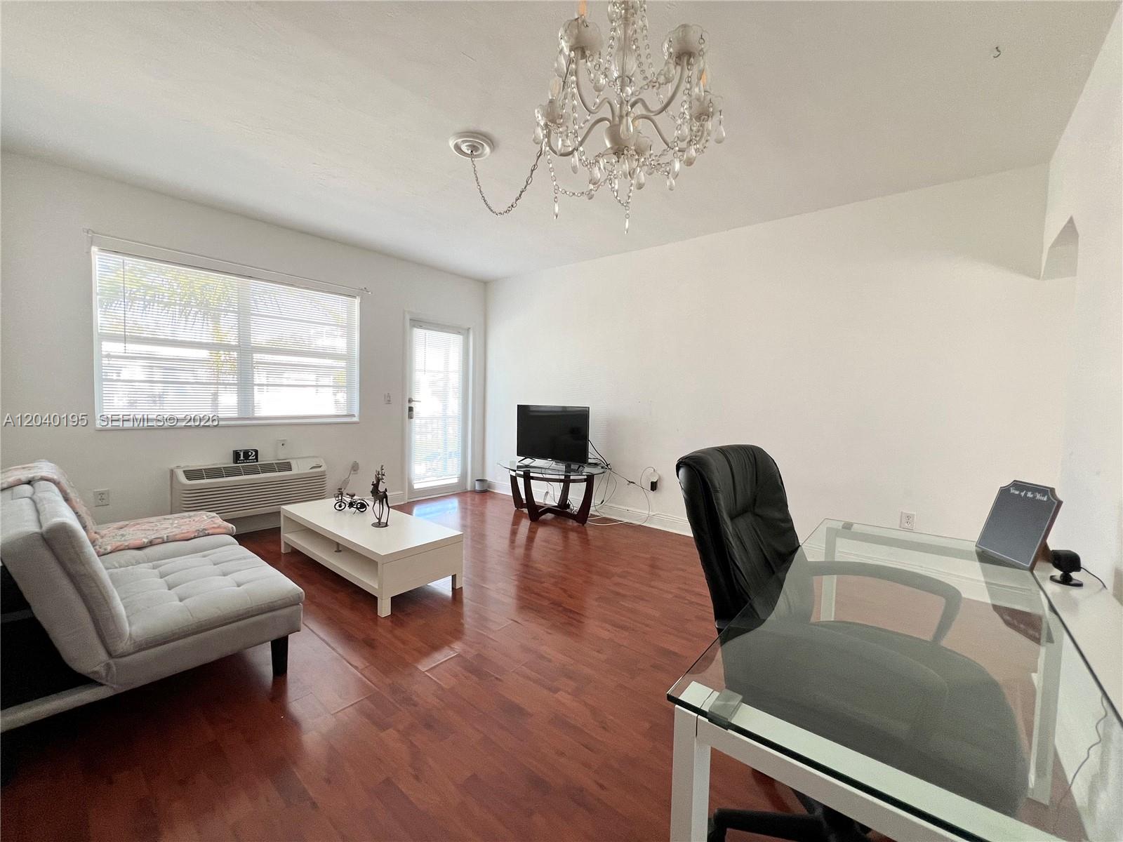 A living room features hardwood floors, a chandelier, a sofa, a desk, and a television — 450 77th St # 6, Miami Beach FL 33141, MIAMI BEACH, FL
