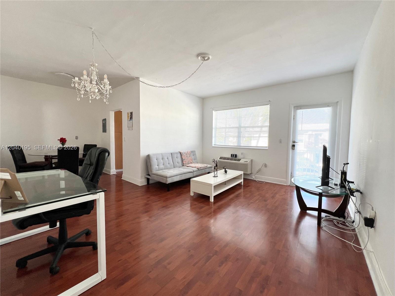 A living room features wood-look flooring, a white sofa, a glass coffee table, and a chandelier — 450 77th St # 6, Miami Beach FL 33141, MIAMI BEACH, FL