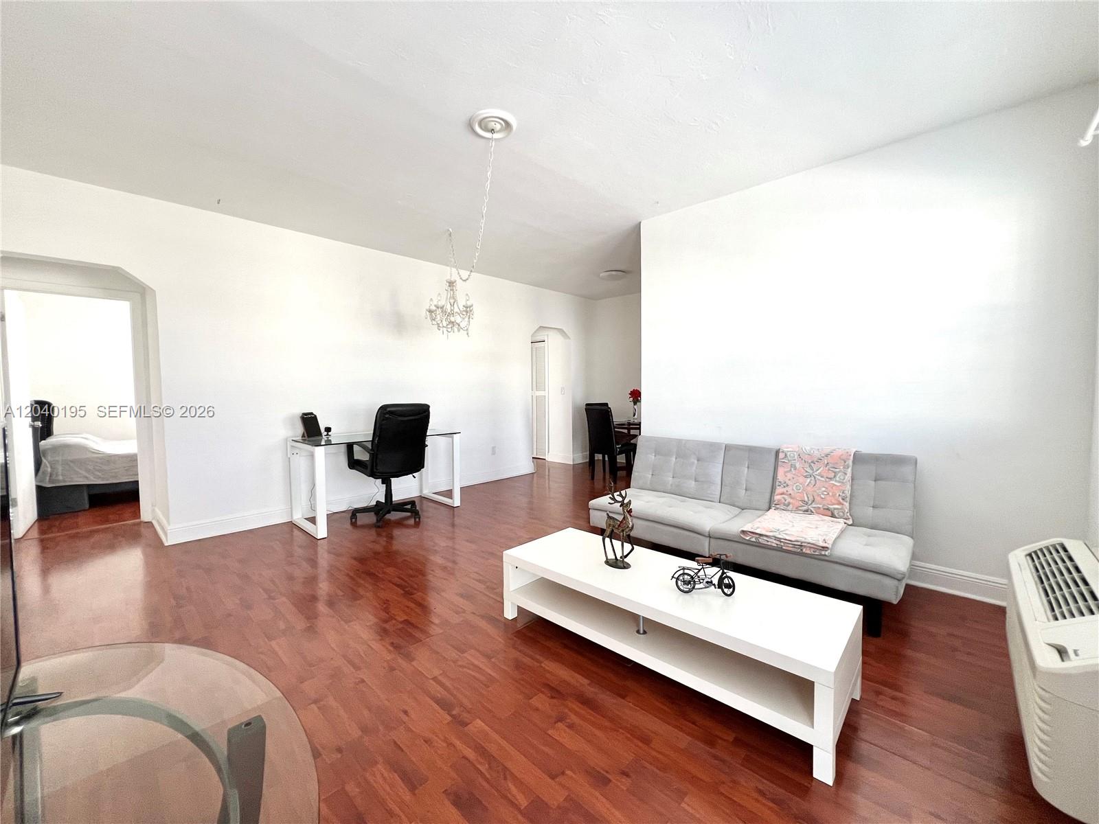 A living room features hardwood floors, a gray sofa, a white coffee table, and desk — 450 77th St # 6, Miami Beach FL 33141, MIAMI BEACH, FL