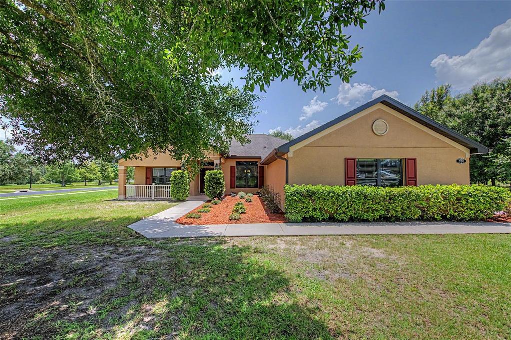A single-story tan house with red shutters, a front porch, and a landscaped yard — 27928 AUSTIN WOODS DRIVE, DADE CITY, FL