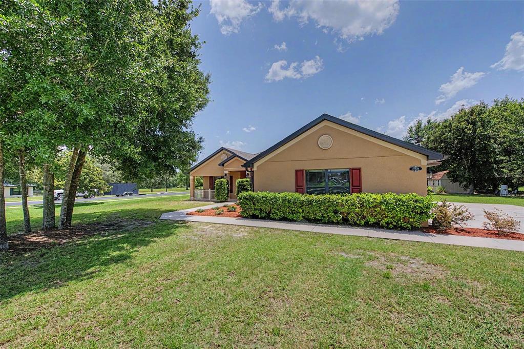 A single-story tan house with a front lawn, sidewalk, and mature trees under a blue sky — 27928 AUSTIN WOODS DRIVE, DADE CITY, FL