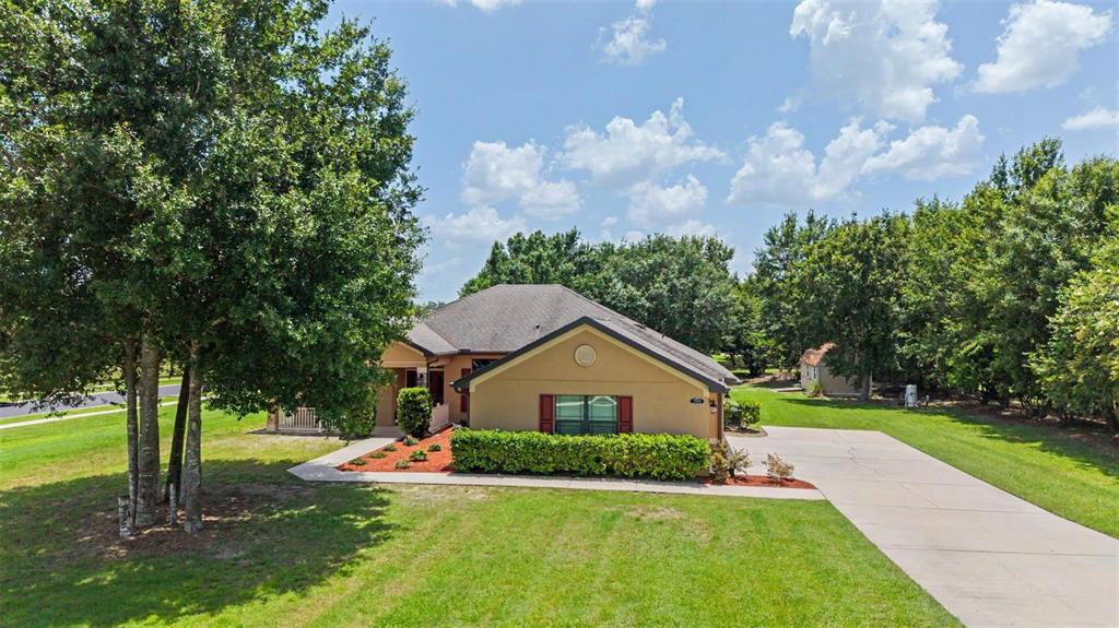A tan single-story house with a concrete driveway, a front hedge, and mature trees — 27928 AUSTIN WOODS DRIVE, DADE CITY, FL