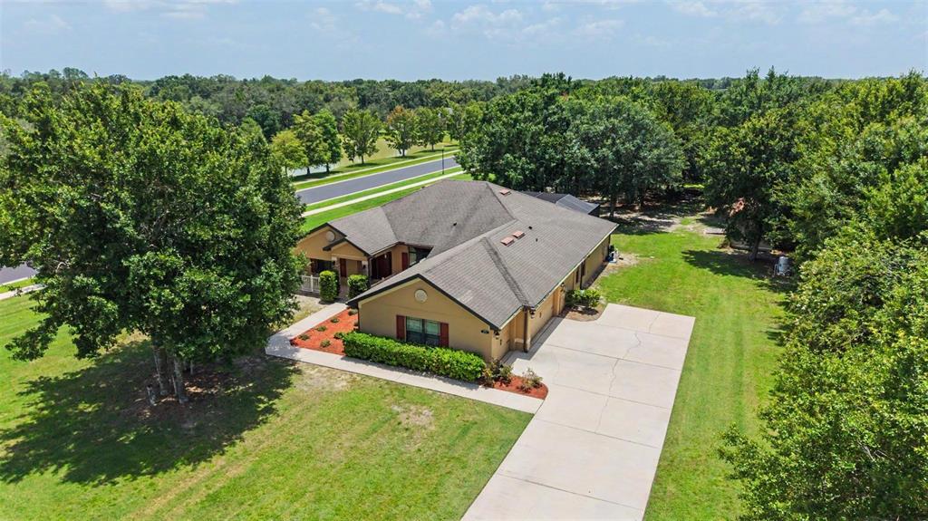 An aerial view shows a single-story house with a concrete driveway and surrounding trees — 27928 AUSTIN WOODS DRIVE, DADE CITY, FL