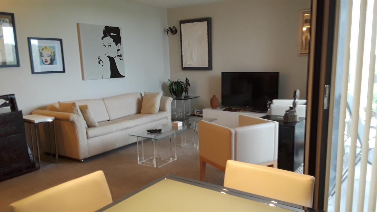 A living room features a beige sofa, glass coffee tables, and framed wall art — 2255 Lindell Boulevard # 4511, Delray Beach FL 33444, DELRAY BEACH, FL