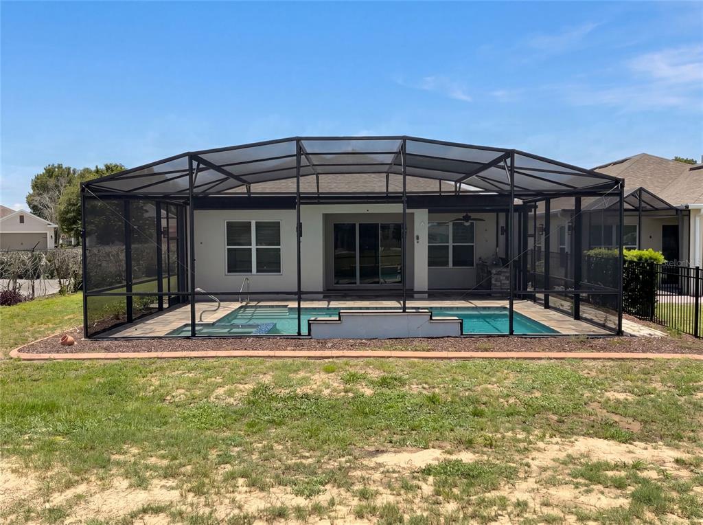 A backyard view of a house with a swimming pool enclosed by a screen cage — 2185 ANTILLES CLUB DRIVE, KISSIMMEE, FL