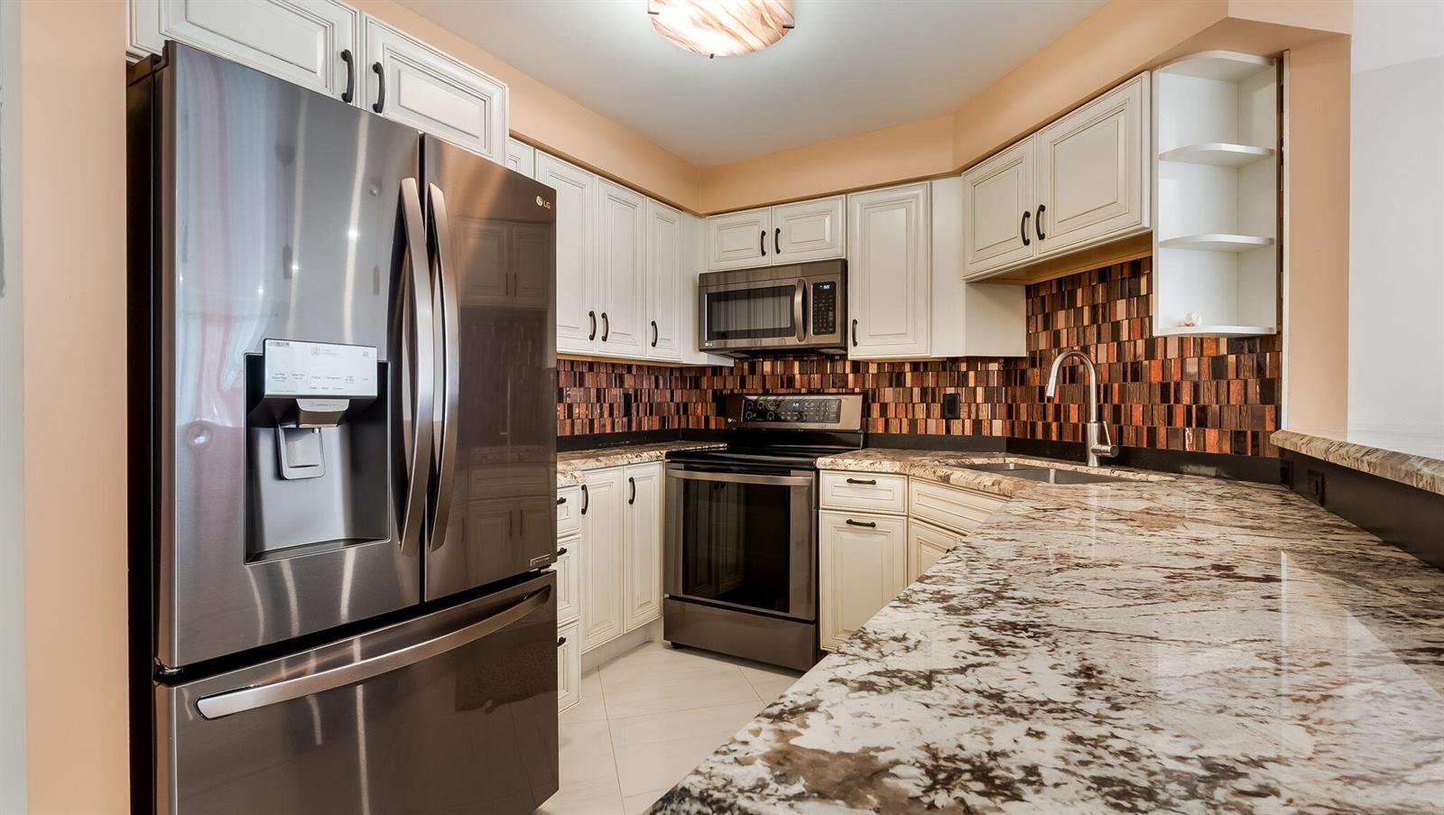 A kitchen features stainless steel appliances, white cabinetry, granite countertops, and a brown tiled backsplash — 133 N Pompano Beach Boulevard # 204, Pompano Beach FL 33062, POMPANO BEACH, FL