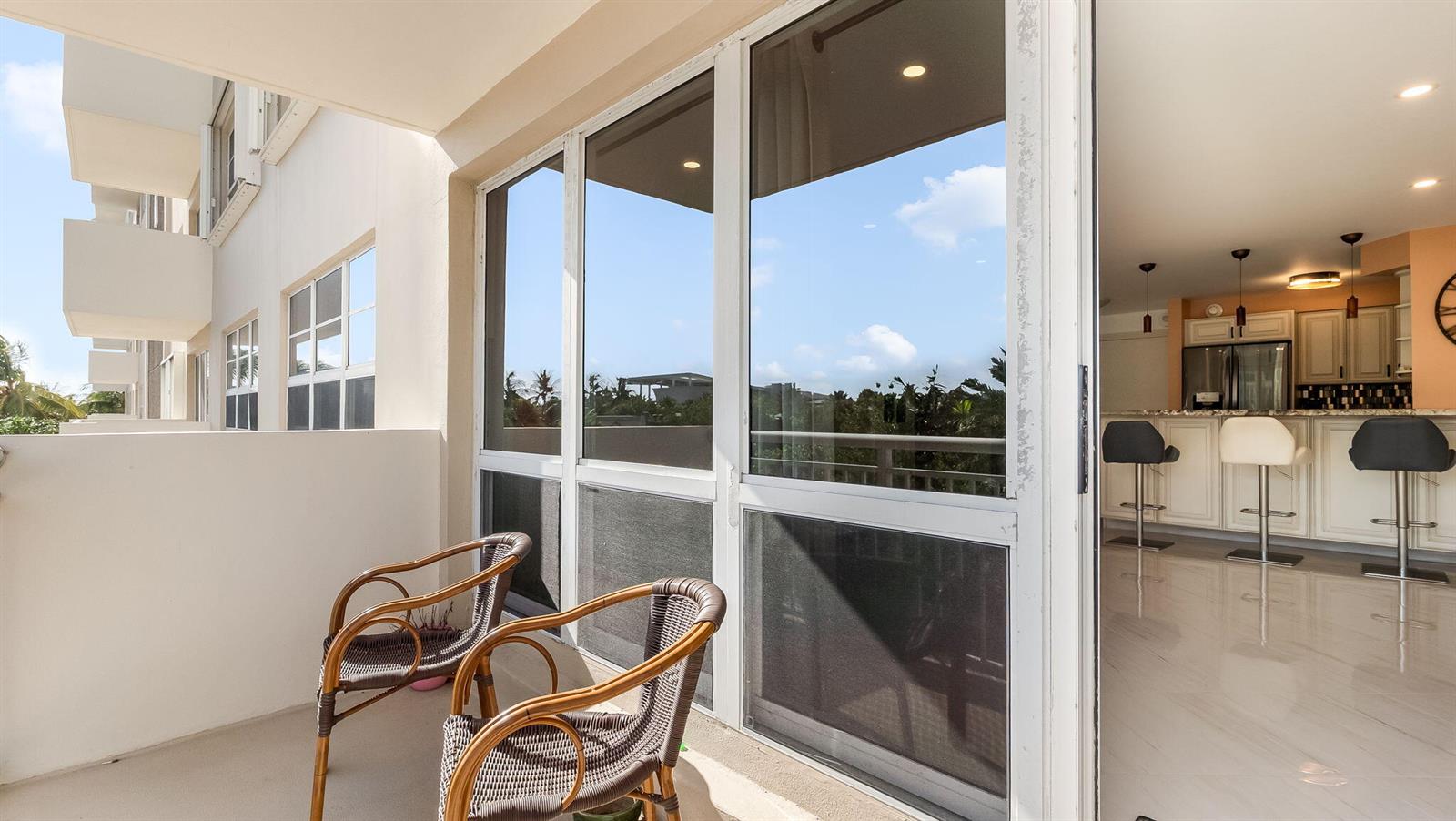 A balcony with two wicker chairs overlooks a kitchen with a breakfast bar and stools — 133 N Pompano Beach Boulevard # 204, Pompano Beach FL 33062, POMPANO BEACH, FL