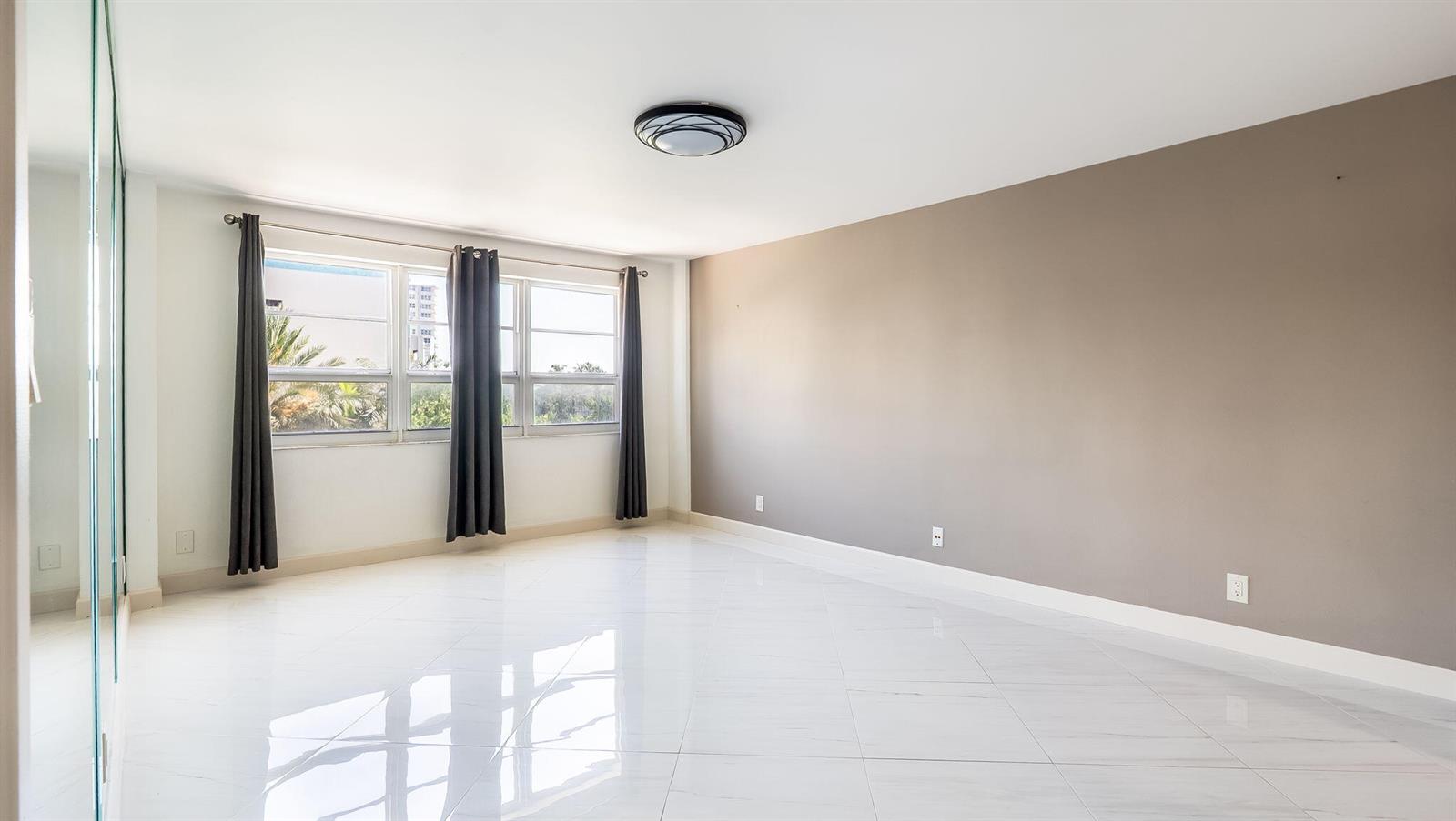 An empty room with white tile floors, a gray accent wall, and large windows — 133 N Pompano Beach Boulevard # 204, Pompano Beach FL 33062, POMPANO BEACH, FL