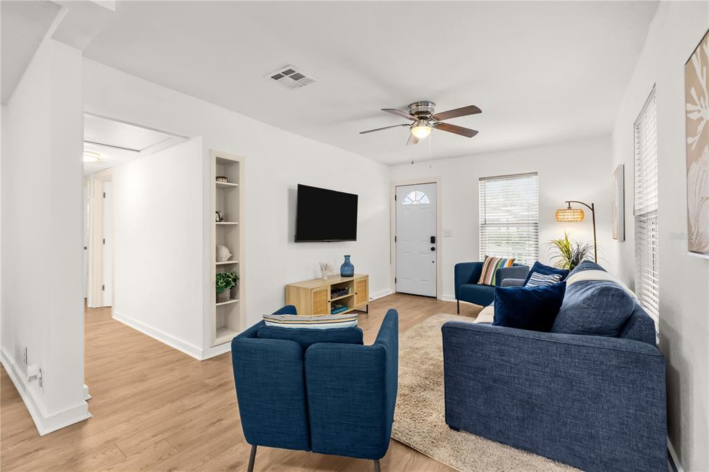 A living room features light wood flooring, blue furniture, a wall-mounted television, and white walls — 3906 N OLA AVENUE, TAMPA, FL