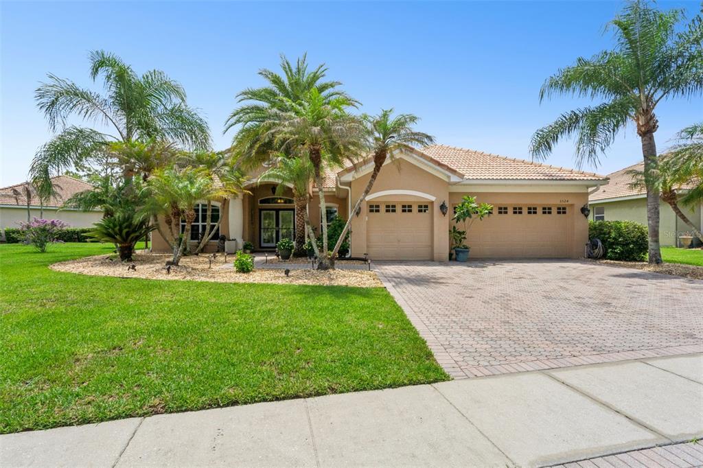 A tan single-story house with a tiled roof, three-car garage, and palm trees in front — 3524 SHOREWOOD DRIVE, KISSIMMEE, FL