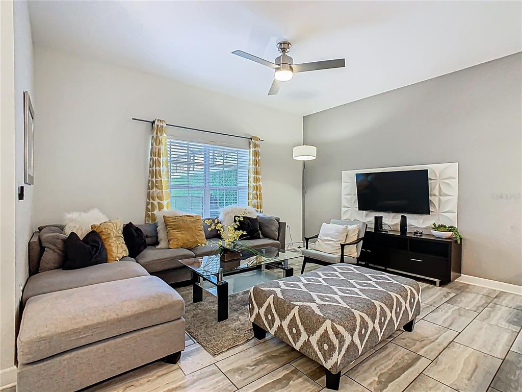 A living room features a gray sectional sofa, a patterned ottoman, and a wall-mounted television — 1579 MOON VALLEY DR, DAVENPORT, FL
