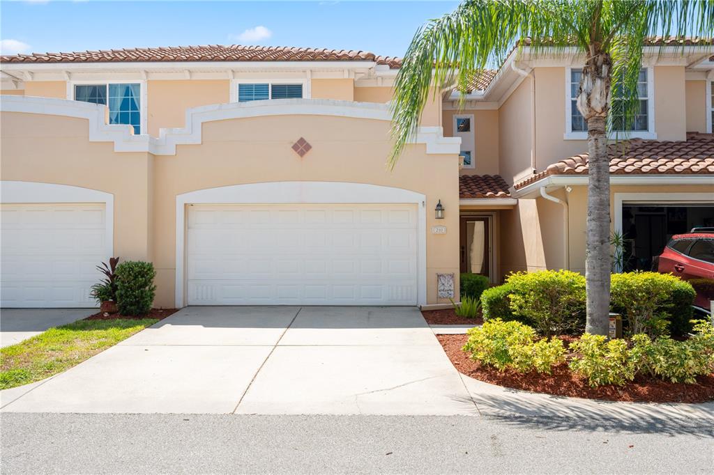 A two-story townhouse exterior features a beige stucco facade, a two-car garage, and a palm tree — 210 VALENCIA CIRCLE, ST PETERSBURG, FL