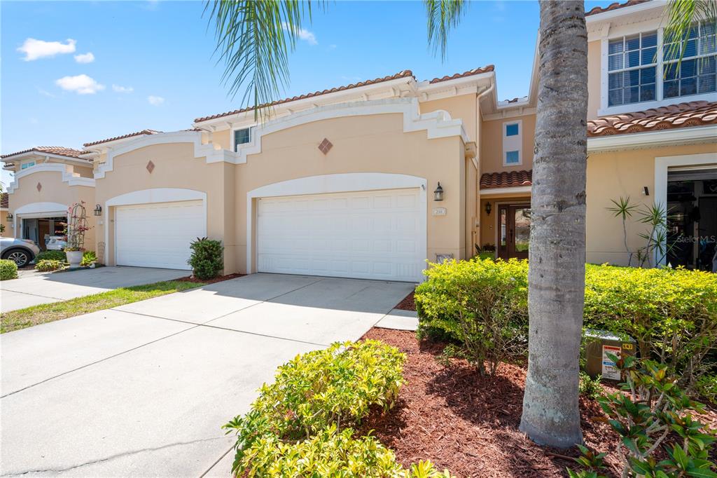 A two-story townhouse exterior features a beige stucco facade, two garage doors, and landscaping — 210 VALENCIA CIRCLE, ST PETERSBURG, FL