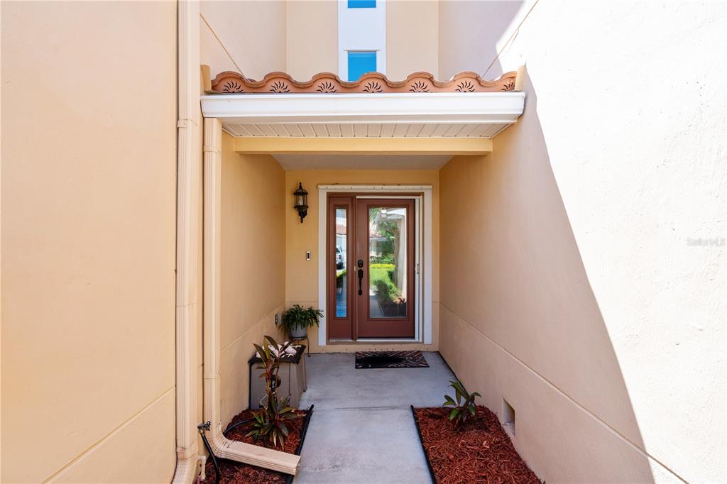 A covered entryway features a brown front door with glass panels and two small garden beds — 210 VALENCIA CIRCLE, ST PETERSBURG, FL