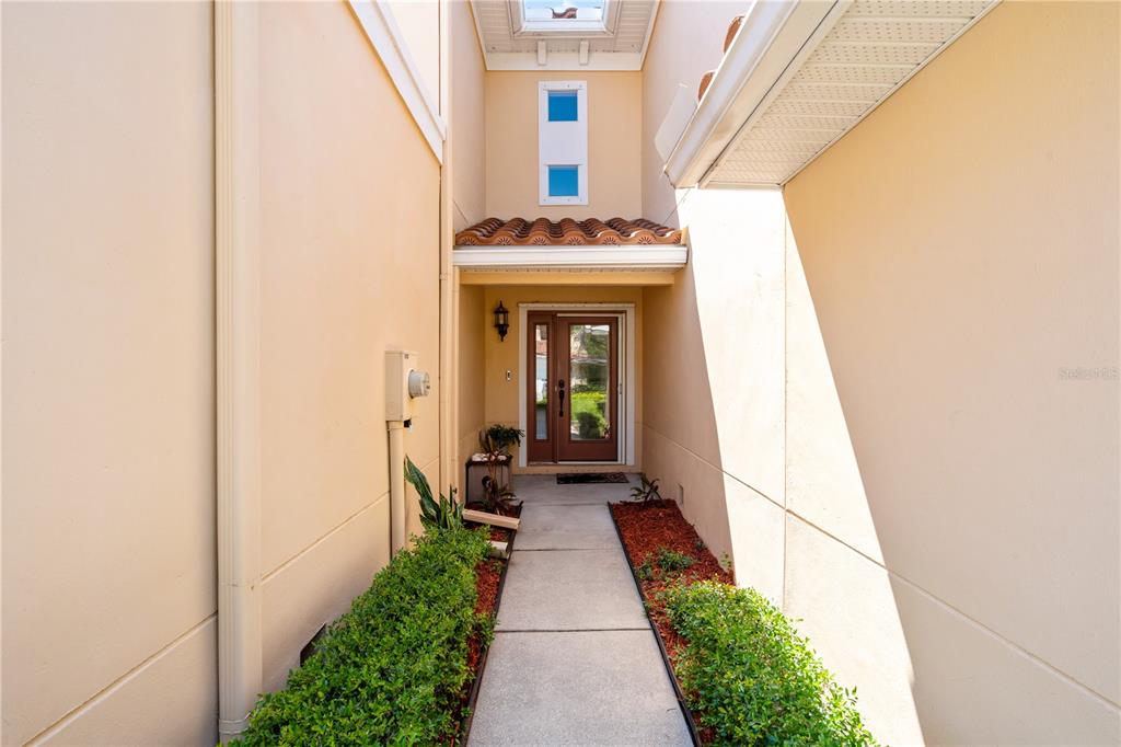 A concrete walkway leads to a front door nestled between two beige exterior walls — 210 VALENCIA CIRCLE, ST PETERSBURG, FL