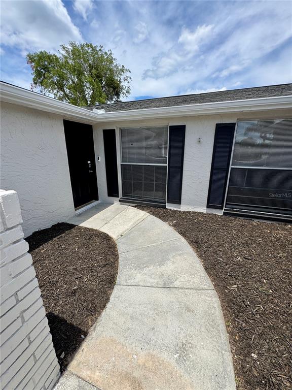 A concrete walkway leads to a black front door beside two windows with black shutters — 6135 SEABREEZE DRIVE, PORT RICHEY, FL
